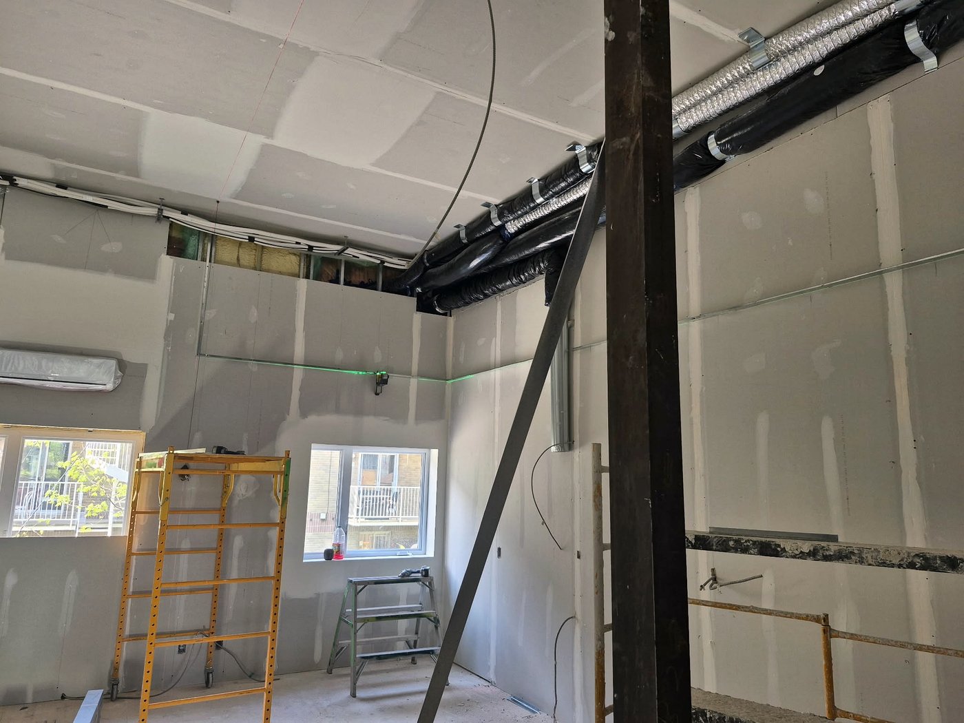 Murs et plafond de gypse avec joints tirés, isolation en mousse dans la retombée et niveau laser projetant une ligne verte — Descoteaux Acoustique